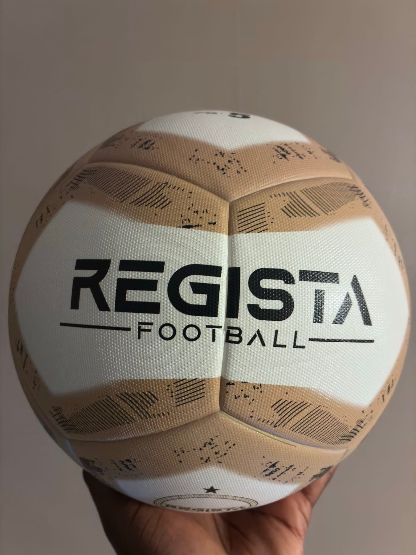 The Regista Training Ball, white with gold panel blocks and the Regista Football wordmark facing the camera.